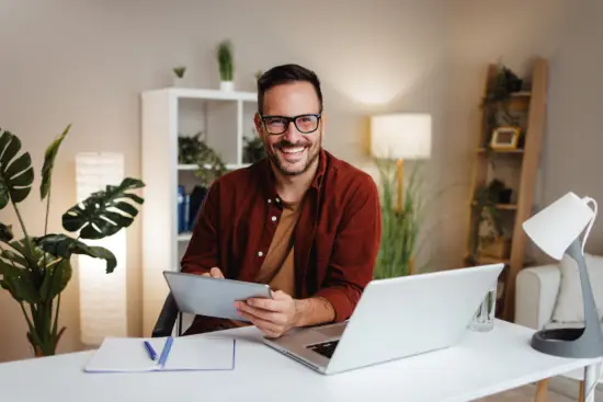 Mann mit Tablet und Laptop sitzt am Schreibtisch