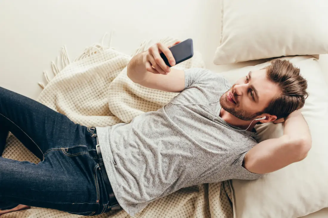 Junger Mann liegt mit Handy auf Sofa